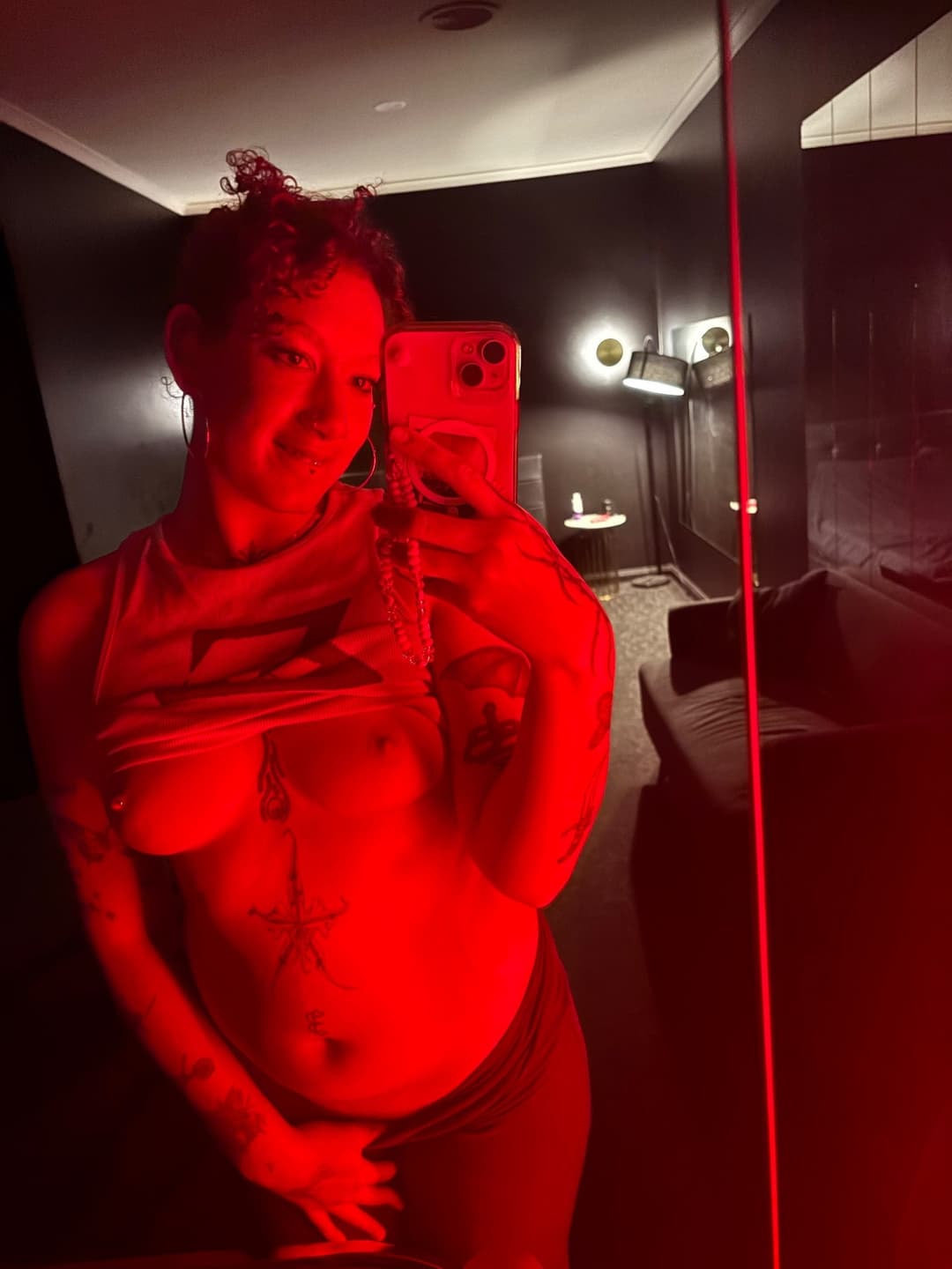 Azara Sin taking a red-lit mirror selfie in a private indoor setting during a sensual, tantra-inspired moment in Melbourne