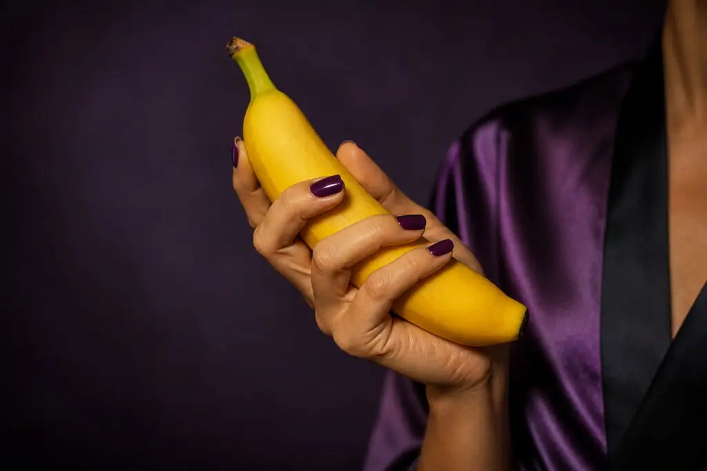 Woman in purple silk robe holding a banana — playful image for happy ending massage guide Australia