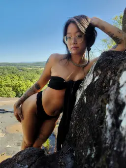 Erotic massage Maroochydore, dark haired woman in glasses leaning on a boulder under blue sky Erotic massage Maroochydore, dark haired woman in glasses leaning on a boulder under blue sky